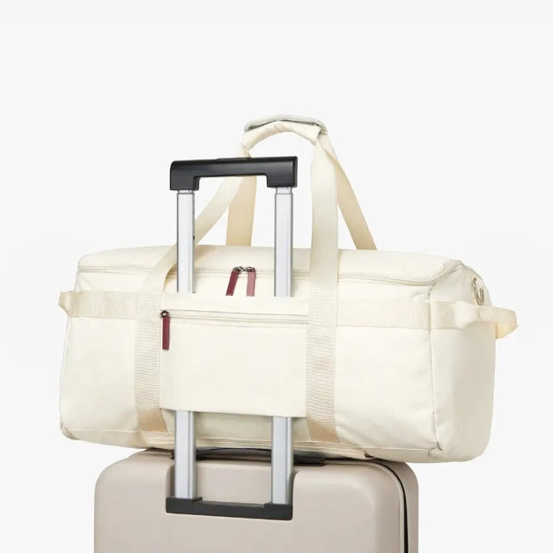Front view of a cream RoamiBag duffel with a pull handle and zipped pockets, on a white background